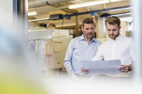 Zwei Männer studieren einen Plan in einer Fabrik - DIGF09998