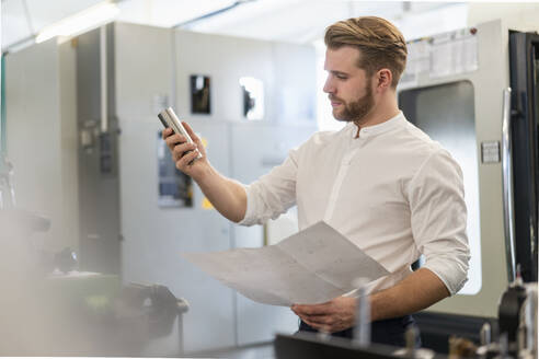 Mann mit Plan und Werkstück in einer Fabrik - DIGF10011