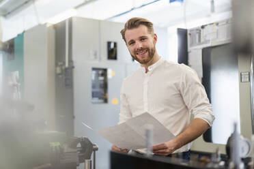 Porträt eines lächelnden jungen Mannes mit einem Plan in einer Fabrik - DIGF10012