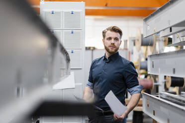 Junger Mann mit Papieren in einer Fabrik - DIGF10021