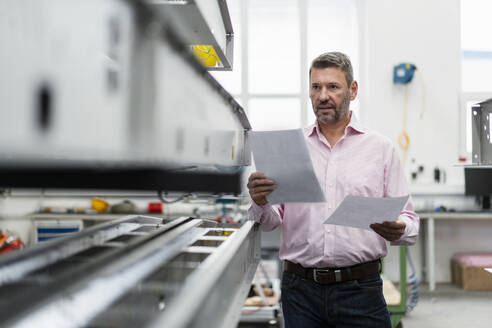 Älterer Mann hält Papiere in einer Fabrik - DIGF10025