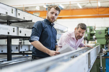 Two men examining piece of metal in a factory - DIGF10032