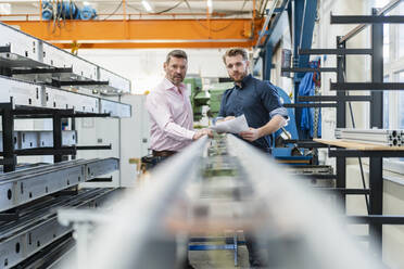 Two men examining piece of metal in a factory - DIGF10035