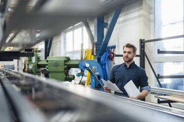 Junger Mann mit Papieren in einer Fabrik - DIGF10038