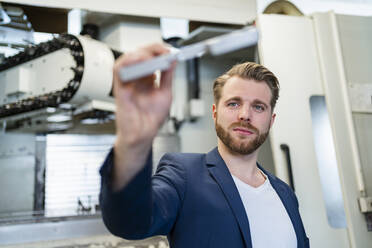 Junger Mann hält ein Werkstück in einer Fabrik - DIGF10052