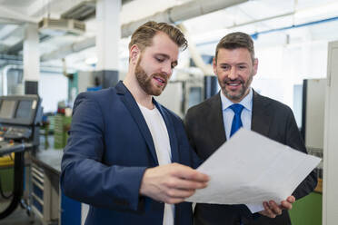 Zwei Geschäftsleute bei einer Arbeitssitzung in einer Fabrik, die einen Plan besprechen - DIGF10058