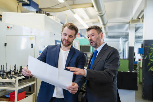 Zwei Geschäftsleute bei einer Arbeitssitzung in einer Fabrik, die einen Plan besprechen - DIGF10060