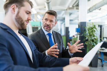 Two businessmen having a work meeting in a factory discussing a plan - DIGF10063