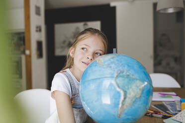 Portrait of confident girl with globe at home looking at distance - HMEF00918