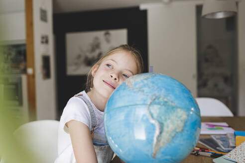 Porträt eines träumenden Mädchens zu Hause, das sich auf einen Globus stützt - HMEF00919