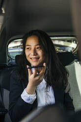 Porträt einer glücklichen Geschäftsfrau, die in einem Auto sitzt und ein Mobiltelefon benutzt - XLGF00112