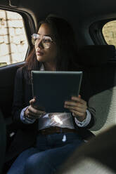 Portrait of young businesswoman with digital tablet sitting in car looking out of window - XLGF00114
