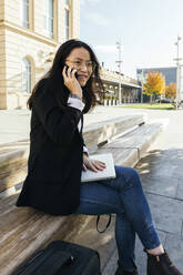Portrait of smiling businesswoman on the phone sitting on bench outdoors - XLGF00121