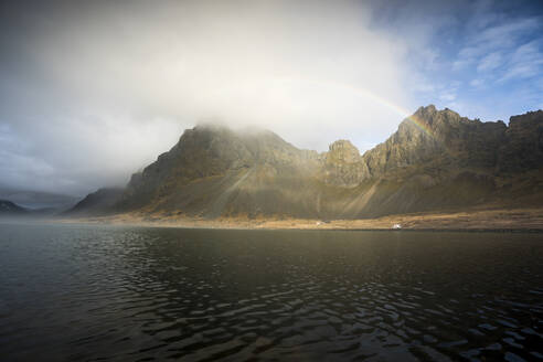 Blick auf die Berge am Wasser gegen den wolkenverhangenen Himmel im Hvalnes Naturreservat Strand - DAMF00420