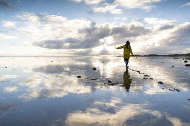 Frau beim Spaziergang im Meer mit Spiegelung am Strand des Naturreservats Hvalnes, Island - DAMF00426