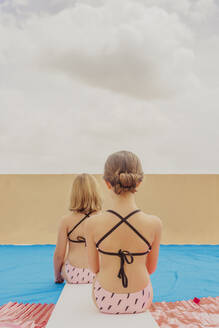 Rückansicht von zwei Mädchen, die auf der Dachterrasse im Schwimmbad spielen - ERRF03590
