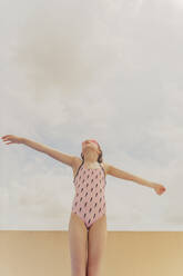 Mädchen mit rosa Badeanzug und Schwimmbrille steht vor einem bewölkten Himmel und schaut nach oben - ERRF03612