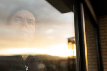 Portrait of serious mature man looking out of window at sunset - VABF02840