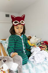 Portrait of little girl with fox mask crouching on bunk bed at home - VABF02842