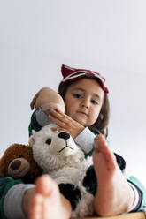 Little girl with cuddly toys showing band-aid on her elbow - VABF02843