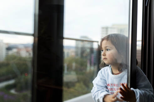 Porträt eines ernsten kleinen Mädchens auf einem Balkon mit Blick in die Ferne - VABF02853