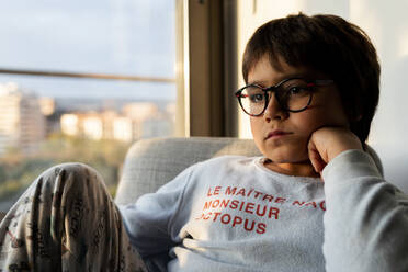 Portrait of bored boy sitting on armchair at home - VABF02859