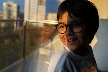 Portrait of happy boy looking out of window at evening twilight - VABF02862