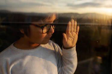 Portrait of little boy behind windowpane watching sunset - VABF02864