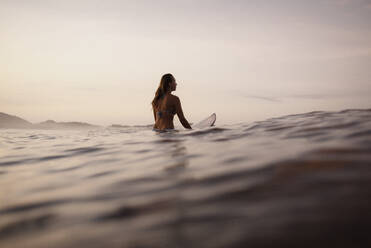 Weibliche Surferin auf dem Surfbrett sitzend am Abend, Costa Rica - HWHF00009