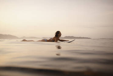 Weibliche Surferin auf dem Surfbrett liegend am Abend, Costa Rica - HWHF00010