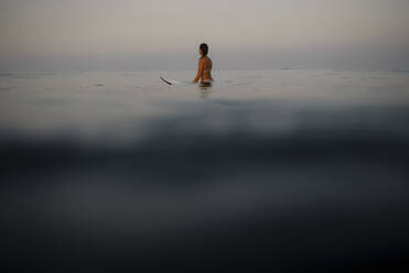 Weibliche Surferin auf dem Surfbrett sitzend am Abend, Costa Rica - HWHF00013