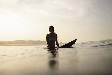 Female surfer sitting on surfboard in the evening, Costa Rica - HWHF00014