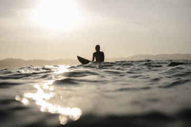 Weibliche Surferin auf dem Surfbrett sitzend am Abend, Costa Rica - HWHF00016