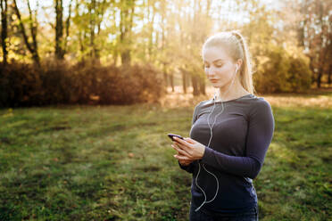 Fitness in the park.Girl holds smartphone and headphones in her hand. - CAVF80536