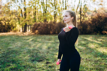 Athletisches Mädchen macht Fitness im Freien mit Hanteln, Seitenansicht. - CAVF80551