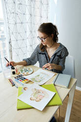 Millennial-Mädchen malt fabelhafte Bilder auf Papier, während sie zu Hause sitzt - CAVF80607