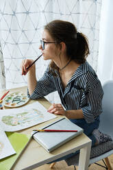 Millennial-Mädchen malt fabelhafte Bilder auf Papier, während sie zu Hause sitzt - CAVF80608