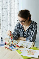 Millennial girl draws fabulous images on paper while sitting at home - CAVF80609