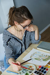 Millennial-Mädchen malt fabelhafte Bilder auf Papier, während sie zu Hause sitzt - CAVF80611