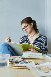 Millennial-Mädchen malt fabelhafte Bilder auf Papier, während sie zu Hause sitzt - CAVF80612