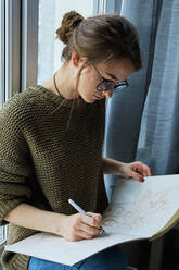 Millennial-Mädchen malt fabelhafte Bilder auf Papier, während sie zu Hause sitzt - CAVF80620
