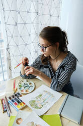Millennial-Mädchen malt fabelhafte Bilder auf Papier, während sie zu Hause sitzt - CAVF80621