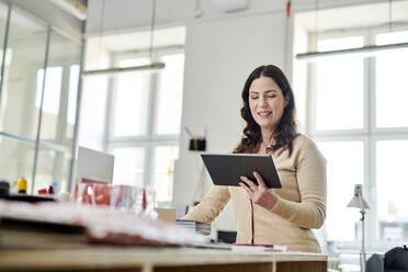 Businesswoman using digital tablet while standing at desk in office - MMIF00216