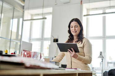 Geschäftsfrau, die ein digitales Tablet im Stehen am Schreibtisch im Büro benutzt - MMIF00216