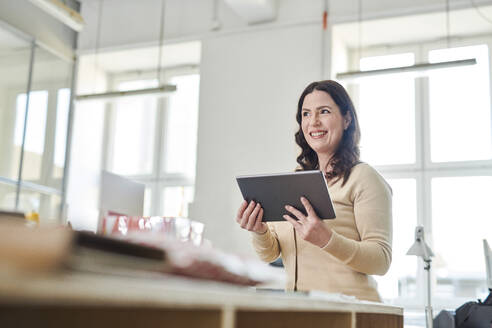 Smiling entrepreneur using digital tablet while standing at desk in workplace - MMIF00217