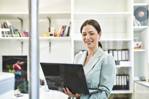 Smiling businesswoman in formals using laptop at office - MMIF00226