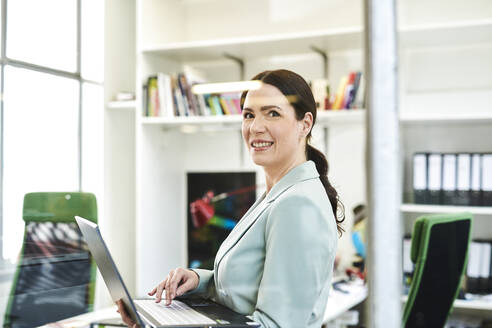 Smiling female professional using laptop while standing at office - MMIF00227