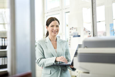 Lächelnder Unternehmer in formeller Kleidung, der am Arbeitsplatz einen Laptop benutzt, lizenzfreies Stockfoto