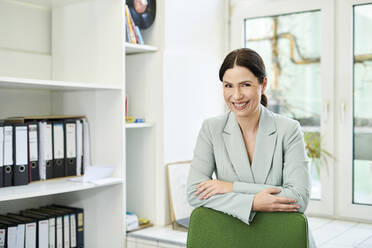 Portrait of smiling businesswoman with arms crossed on chair at office - MMIF00231