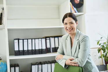 Confident smiling female professional standing on office chair at office - MMIF00233